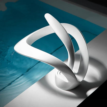 A sleek white ceramic sculpture with smooth curves featured in a deck mounted single hole cold water basin faucet