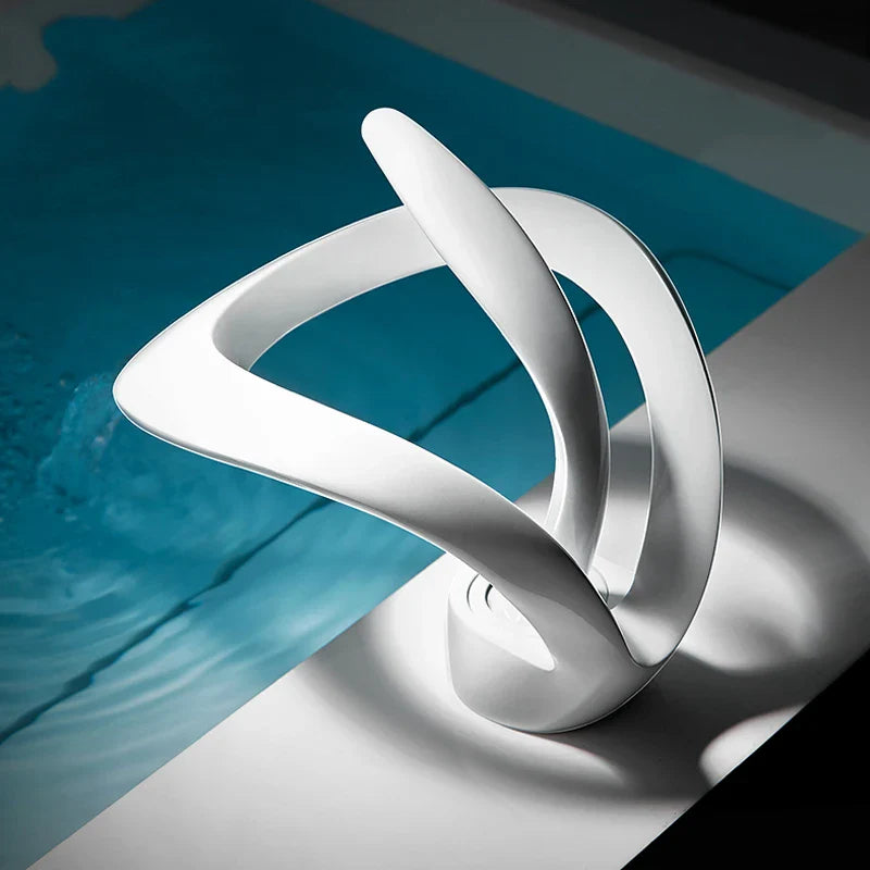 A sleek white ceramic sculpture with smooth curves featured in a deck mounted single hole cold water basin faucet