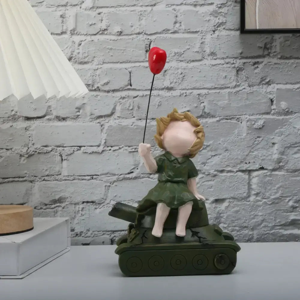 A charming resin balloon girl statue in a green dress holding a red heart balloon atop an olive-green tank for decor