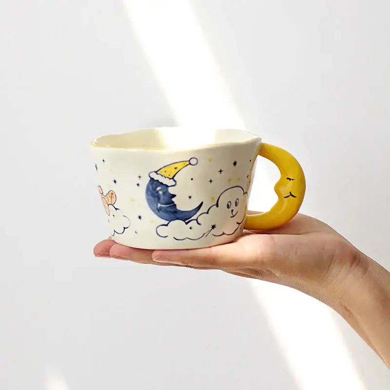 Whimsical off-white bear moon ceramic mug featuring a blue crescent moon and smiling yellow face handle