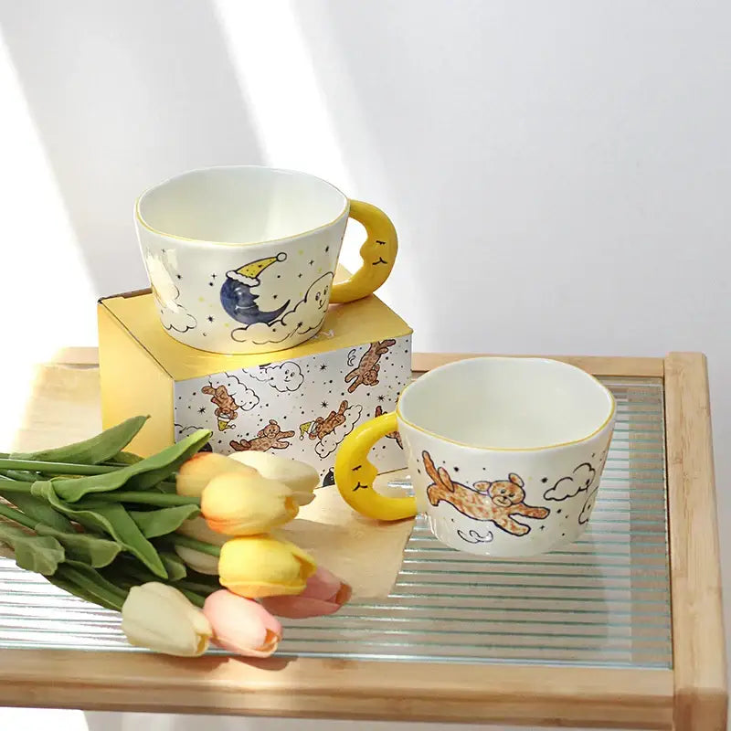 Off-white bear moon ceramic mug with yellow crescent moon handle and whimsical sleeping moon and jumping bear design
