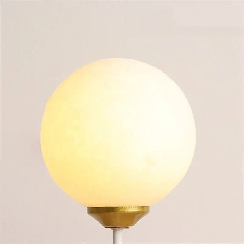 A warm frosted glass globe lamp with a brass metal base in a whimsical pink blue and white bear kids wall lamp set