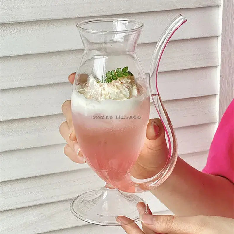 Clear glass vampire cocktail glass cup with curved handle filled with pink layered drink topped with mint leaves
