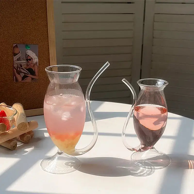 Two clear glass pitchers with curved spouts and long slender straws for whimsical pink vampire cocktail glass cup decor