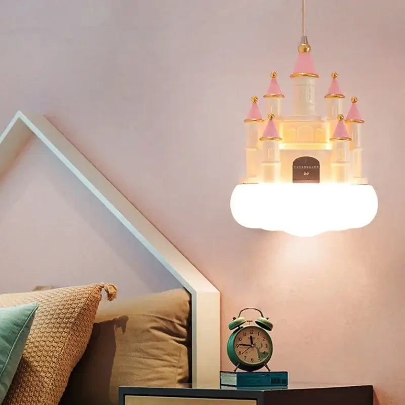 A whimsical pink and white castle kids chandelier led with gold accents hangs above a bedside table for decorbites castle kids