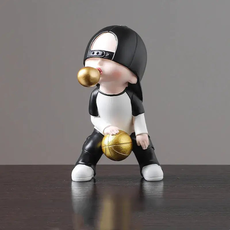 A black and white whimsical resin boys sports statue holding a gold basketball and blowing a golden bubble gum ball