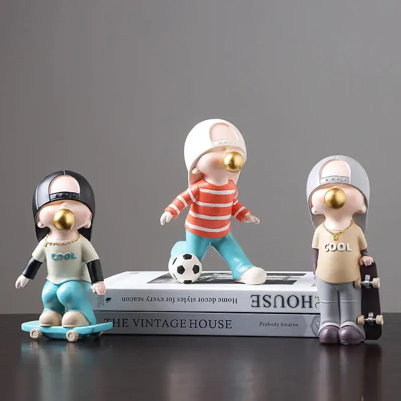 Three whimsical resin boys sports statues with gold bubble noses in colorful sporty outfits on stacked books decorbites boys