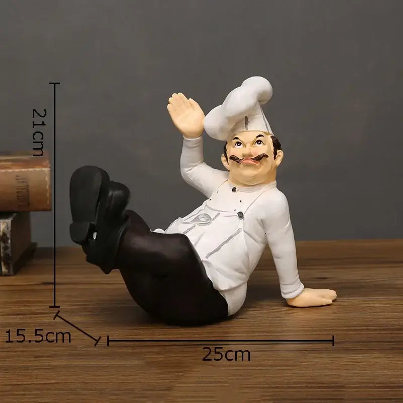 A cheerful white bearded chef resin figure in a white uniform and tall hat waving in a relaxed seated pose for kitchen decor