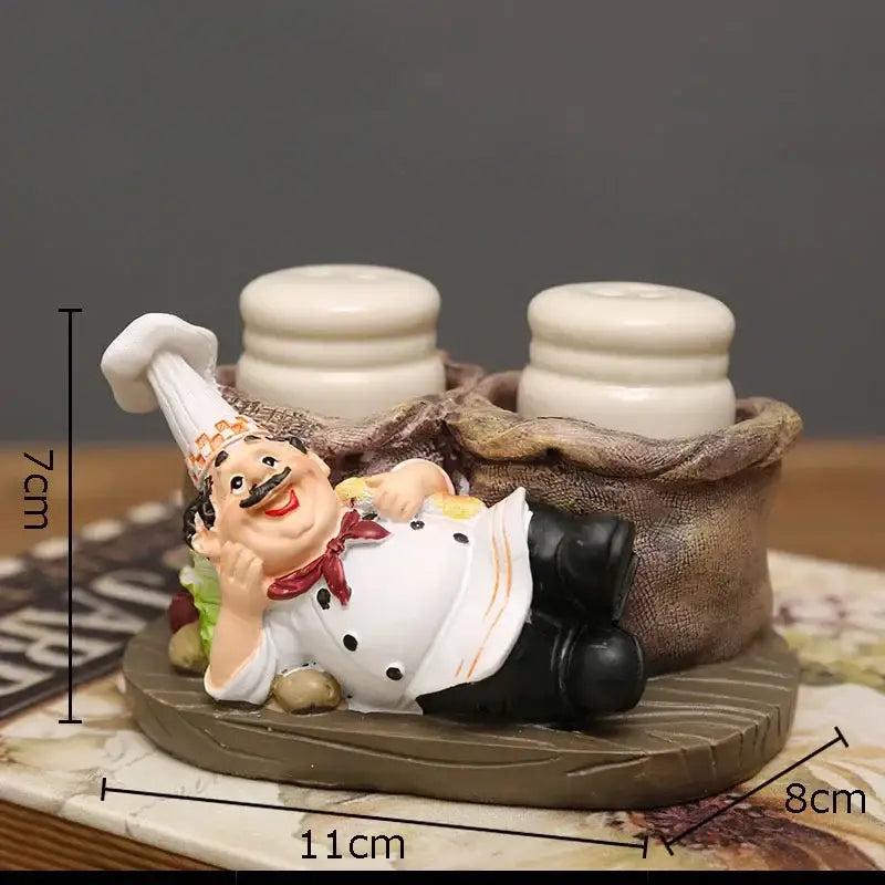 A cheerful white bearded chef resin figure with red bow tie reclining in a sack base holding salt and pepper shakers