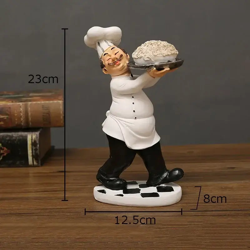 A cheerful white and black bearded chef resin figure wearing a tall hat holding a tray with a decorative pie