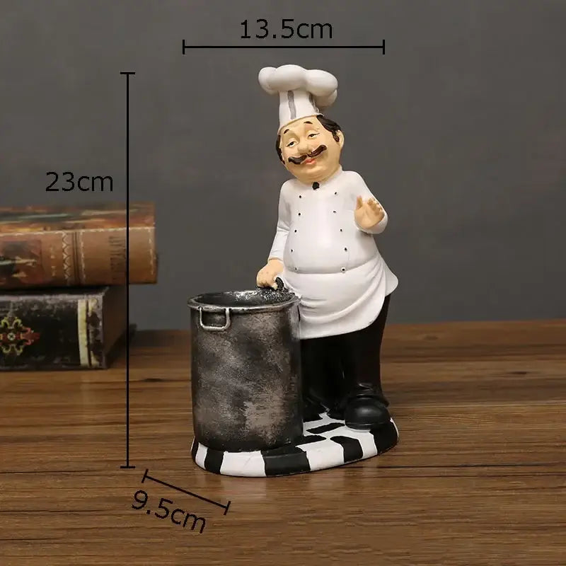 A whimsical white bearded chef resin figure with black mustache and tall hat beside a rustic metallic pot