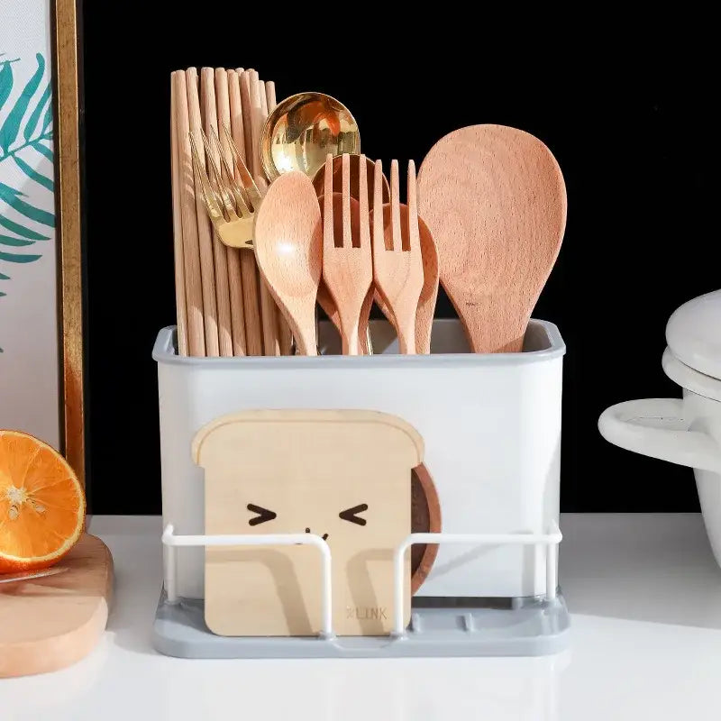 White plastic double grid cutlery organizer with black base and front rack holding beige bread slice cutout with eyes