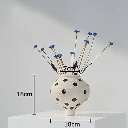 White ceramic vase with black polka dot textured surface holding blue dried flowers for living room decor