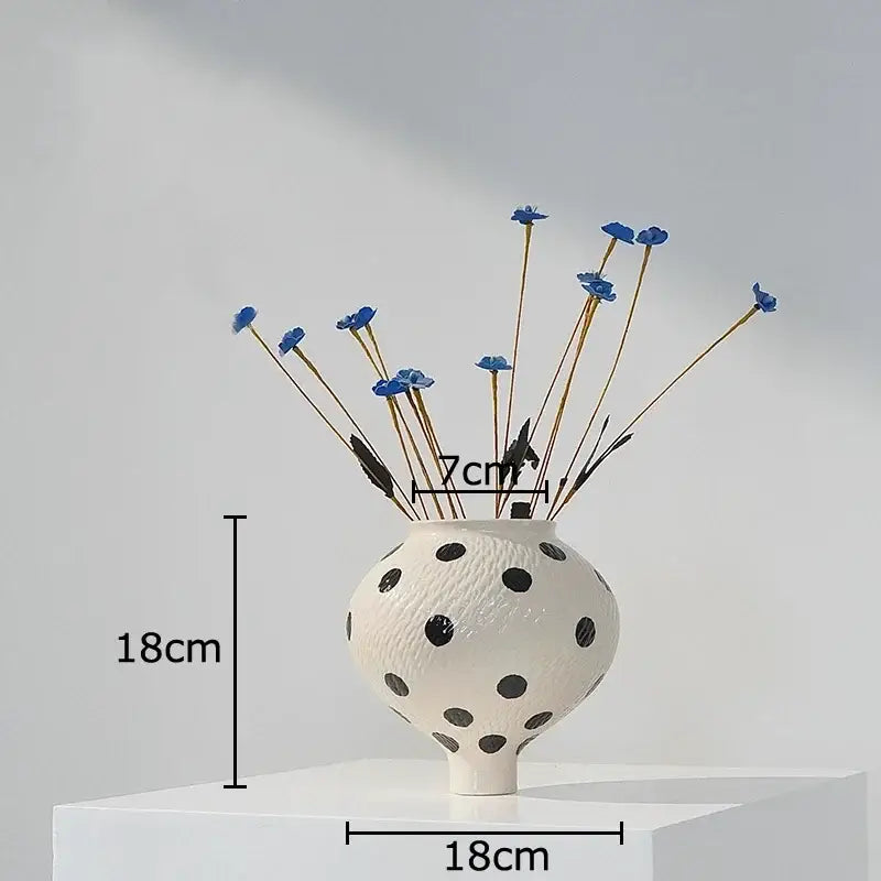 White ceramic vase with black polka dot textured surface holding blue dried flowers for living room decor