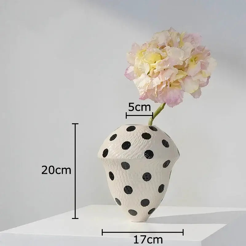 White ceramic wavy vase with black polka dot texture holding pale pink and yellow hydrangeas for living room decor