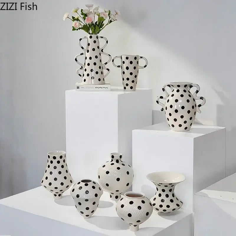 A collection of white ceramic vases with black polka dot wavy sculptural handles displayed on tiered pedestals for living room decor