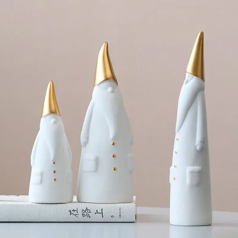 Three white ceramic santa claus figurines with gold-tipped hats and button details for christmas decor