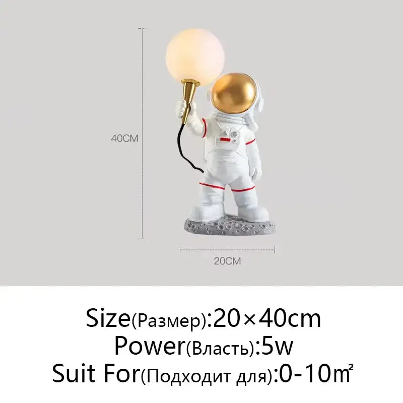 White and gold decorbites astronaut moon lamp with red accents holding glowing sphere on textured gray moon planet table