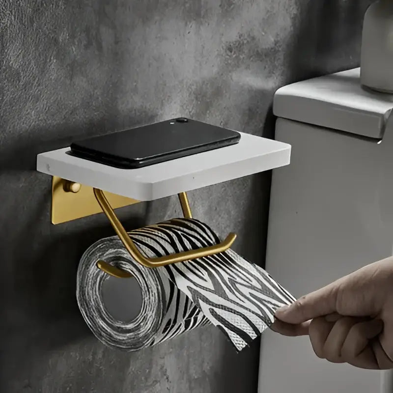 White and gold marble paper holder with a gold marble finish and a white marble shelf holding a black smartphone