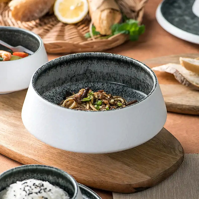 A modern white and grey ceramic bowl with ice cracked glaze and speckled black interior filled with noodles