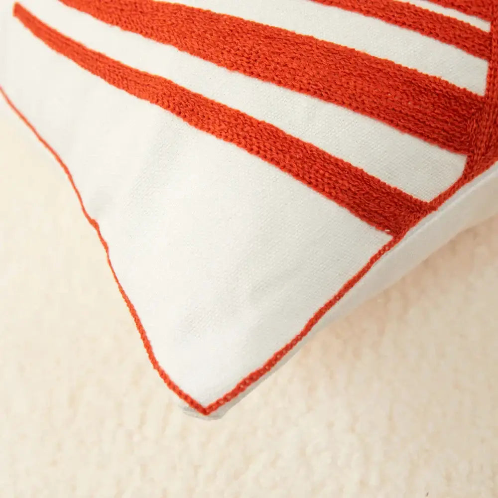 White pillow cover with textured orange stripes and matching stitching complements embroidered leaf pillow for living room