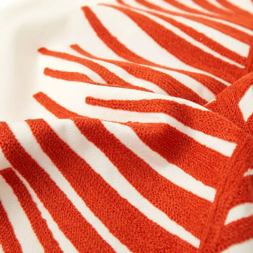 A plush orange and white striped towel with textured terry cloth weave next to a white and olive green embroidered leaf pillow cover
