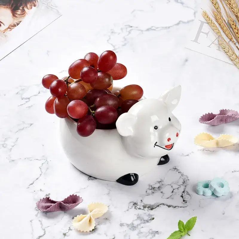 White ceramic pig-shaped fruit bowl with black accents filled with grapes paired with decorbites duck ceramic dessert bowl