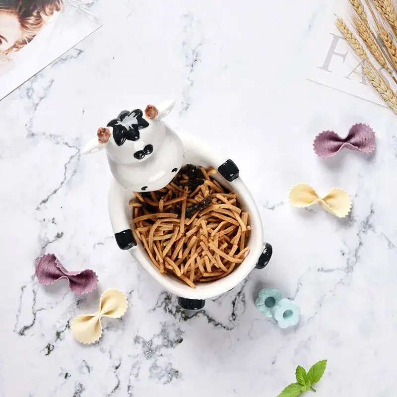 White ceramic cow-shaped bowl with black accents and copper horns filled with noodles for decorbites duck ceramic dessert use