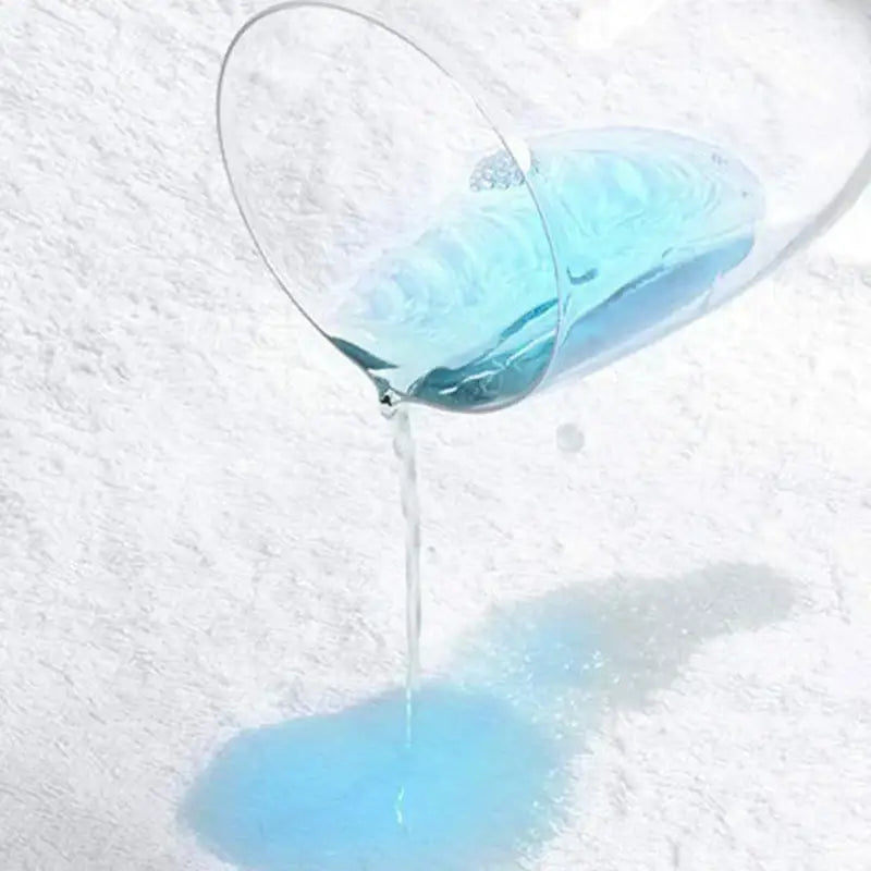 A clear glass beaker pours blue liquid onto a white textured elder hypoallergenic waterproof fitted sheet