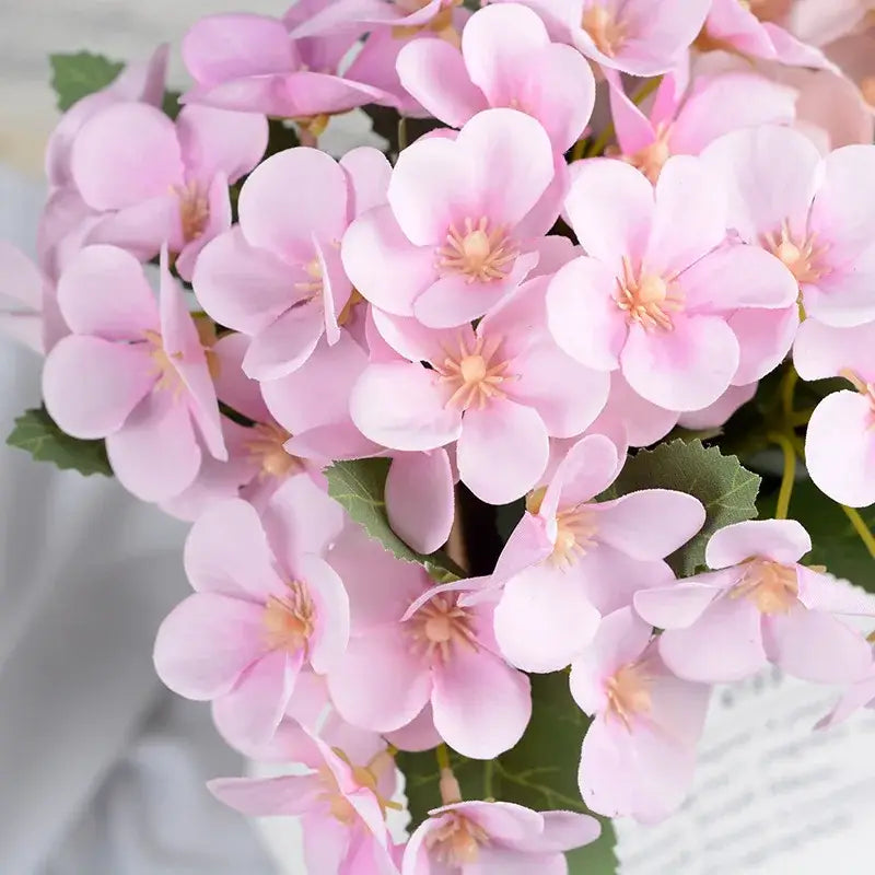 A delicate pink begonia silk flower bouquet with soft layered petals in a white ceramic vase for living room decor