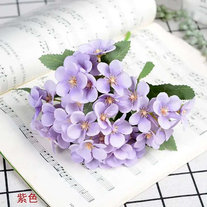 A white begonia silk flower bouquet featuring delicate lavender silk flowers in a ceramic vase for living room decor