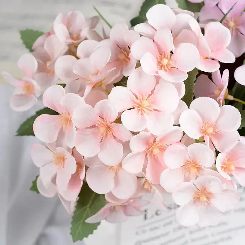 A delicate pink artificial flower bouquet with soft petals and yellow centers in a white begonia silk flower vase decor