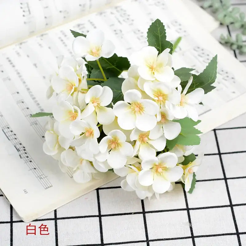 A delicate white begonia silk flower bouquet with yellow centers and green leaves in a ceramic vase for living room decor