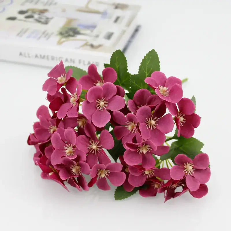 A white begonia silk flower bouquet with magenta silk flowers and green leaves in a ceramic vase for living room decor