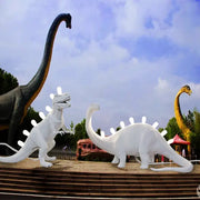 White resin led desk lamp featuring brontosaurus and t-rex dinosaur statues with glowing back spines for bedroom use