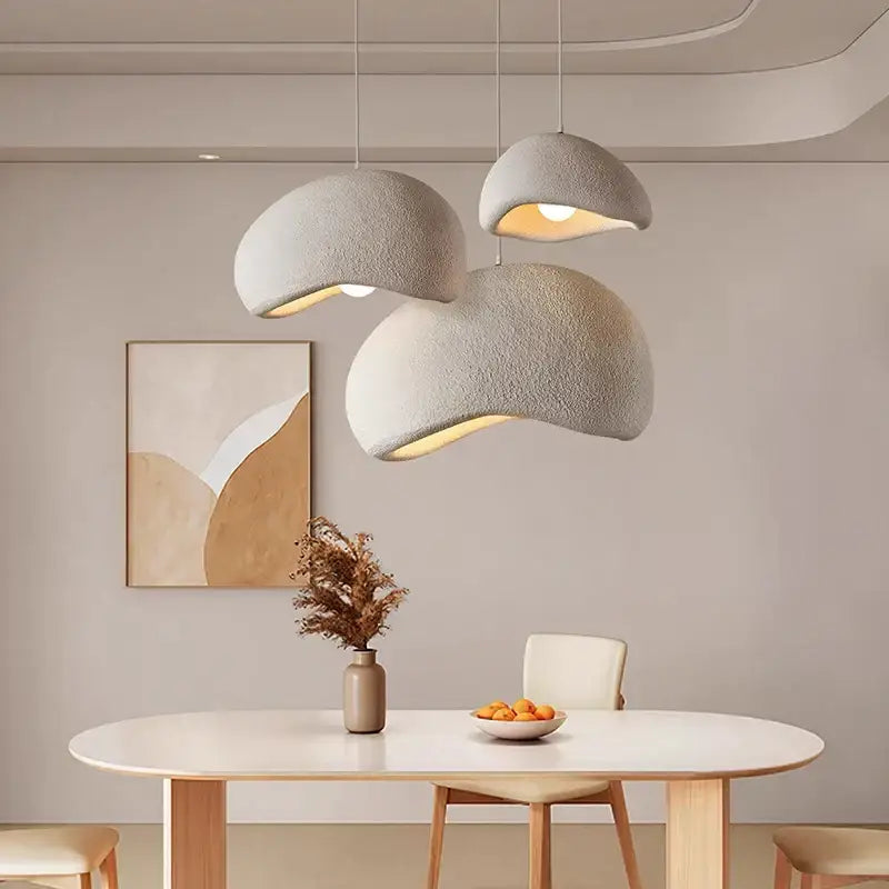 Three modern textured gray cement wind cloud pendant lights hang above a minimalist dining table decorbites cement wind