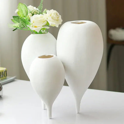 Three elegant white ceramic balloon geometric vases with slender legs holding delicate white roses for living room decor