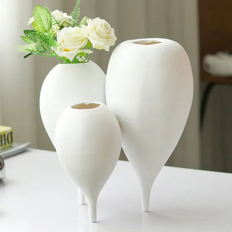 Three elegant white ceramic balloon geometric vases with slender legs holding delicate white roses for living room decor