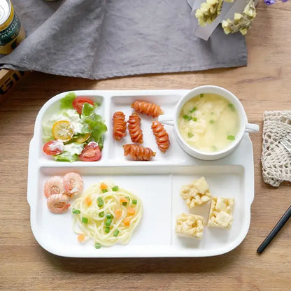 White ceramic decorbites ceramic divided plate with four compartments holding salad pasta shrimp and a bowl of egg soup