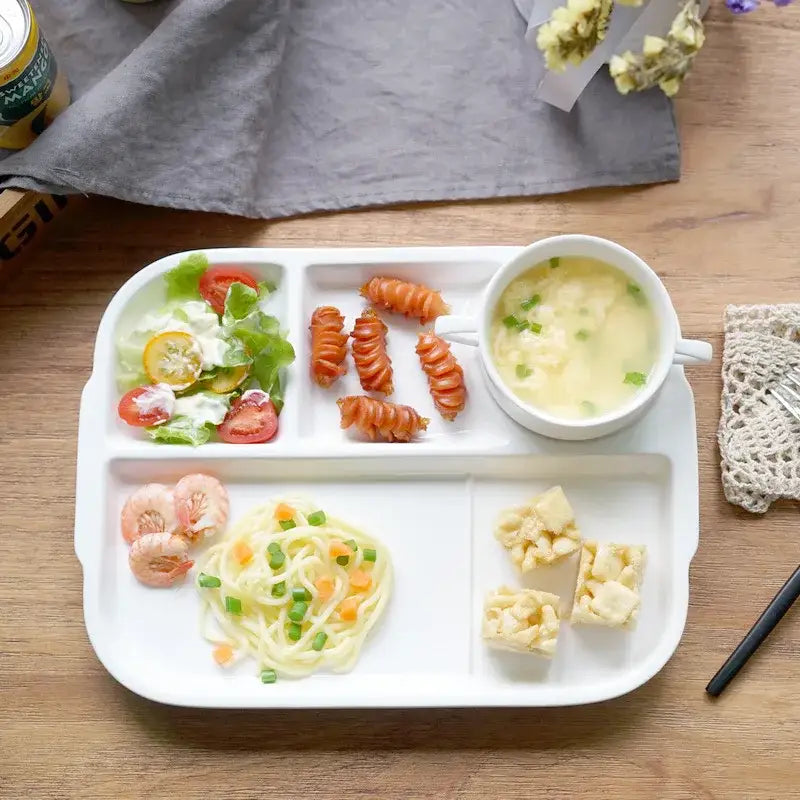 White ceramic decorbites ceramic divided plate with four compartments holding salad pasta shrimp and a bowl of egg soup