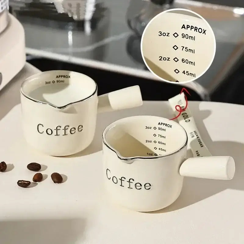 White ceramic espresso measuring cup and milk pitcher with black coffee lettering and silver rim accents for decorbites espresso measuring