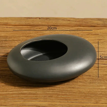 A sleek matte black ceramic ashtray with smooth oval shape and circular opening for decorbites cobblestone deformation decor