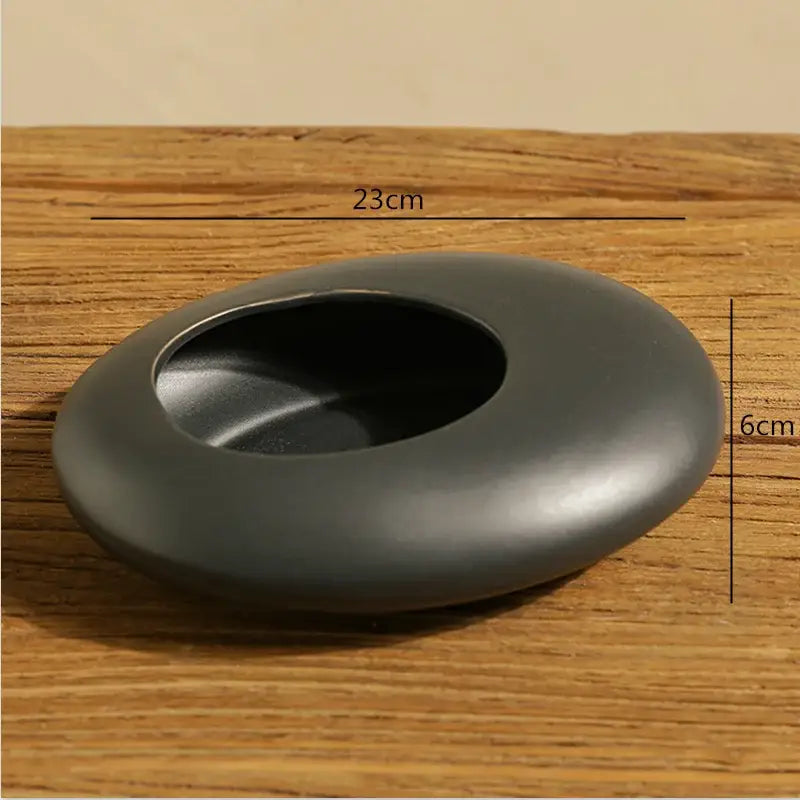 Black smooth ceramic ashtray with central oval opening paired with white cobblestone deformation ceramic vase for decorbites decor