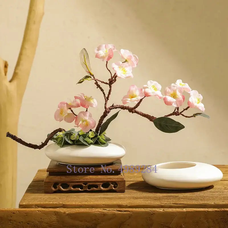 A delicate pink cherry blossom arrangement in a white cobblestone deformation ceramic bonsai pot for living room decor