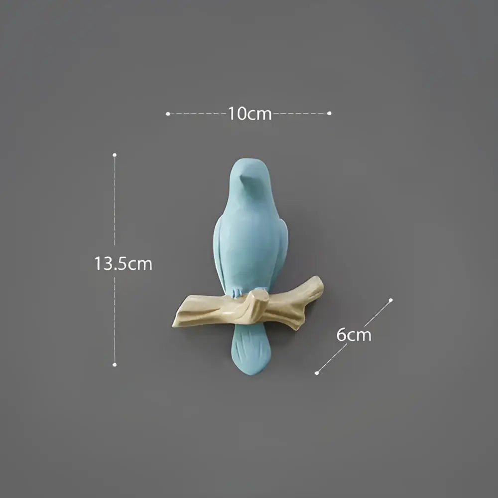 A light blue ceramic decorbites bird resin hanger on a beige wood branch for wall decor and kitchen use