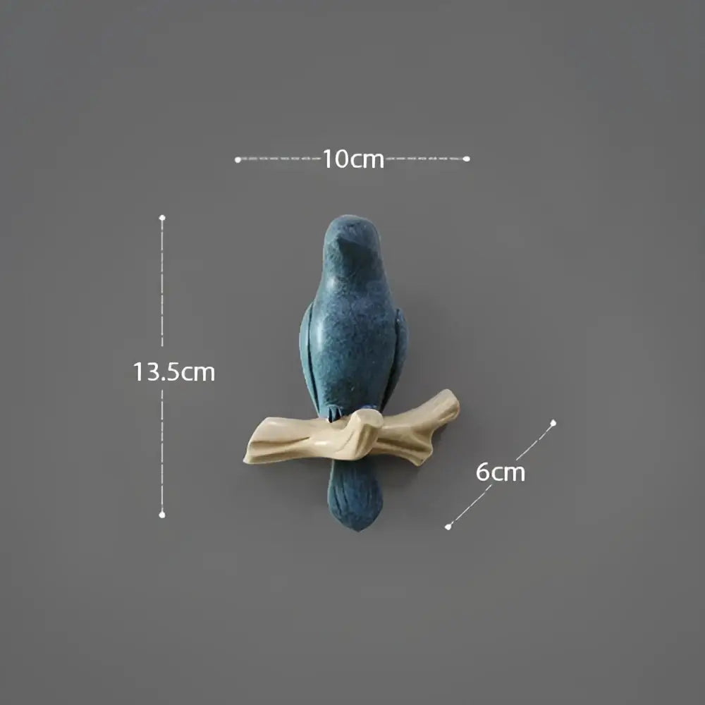 A matte blue ceramic decorbites bird resin figurine perched on a light beige wood branch bird resin hanger
