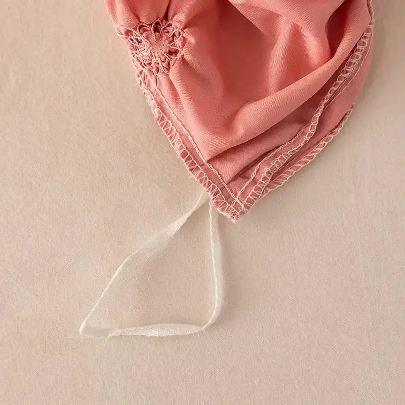 A delicate pink fabric bonnet with lace trim and white ribbon tie shown alongside a white diamond pinch pleated duvet cover set