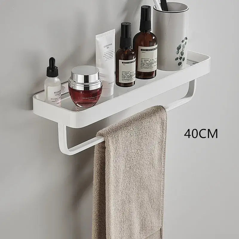White double tier glass corner shelf with towel bar and white plastic wall-mounted towel rack holding beige towel and toiletries
