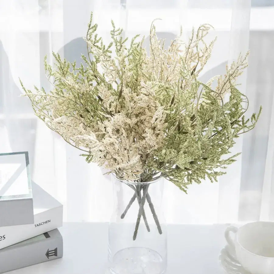 A delicate white dried baby’s breath lavender bouquet with green and cream foliage in a clear glass vase