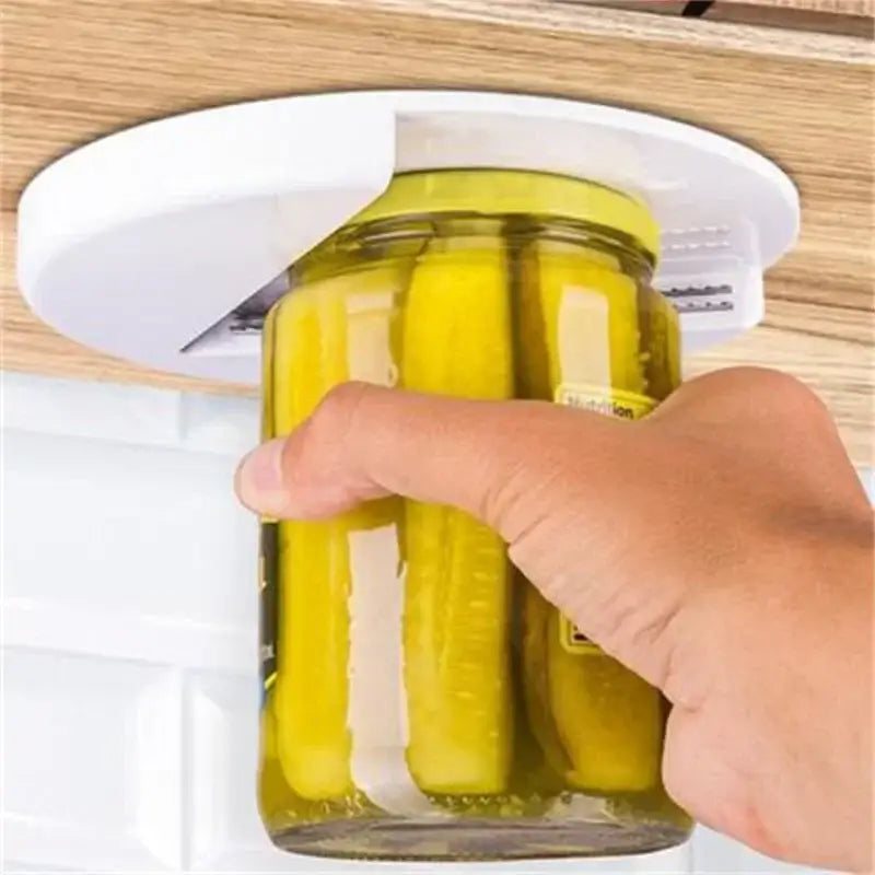 White easy twist jar opener with adhesive mount grips lid of glass jar filled with yellow pickles under wooden countertop